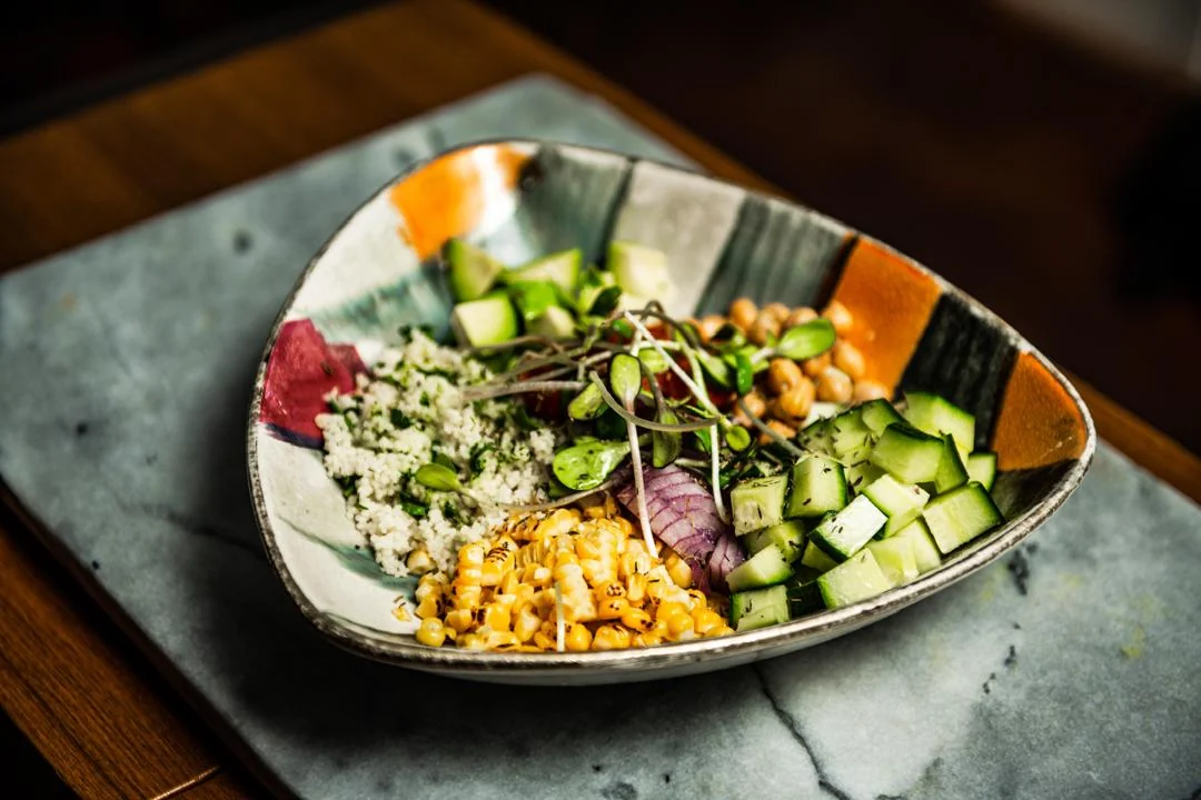 Colourful grain bowl with cucumber, chickpeas and sweetcorn on a stone slab
