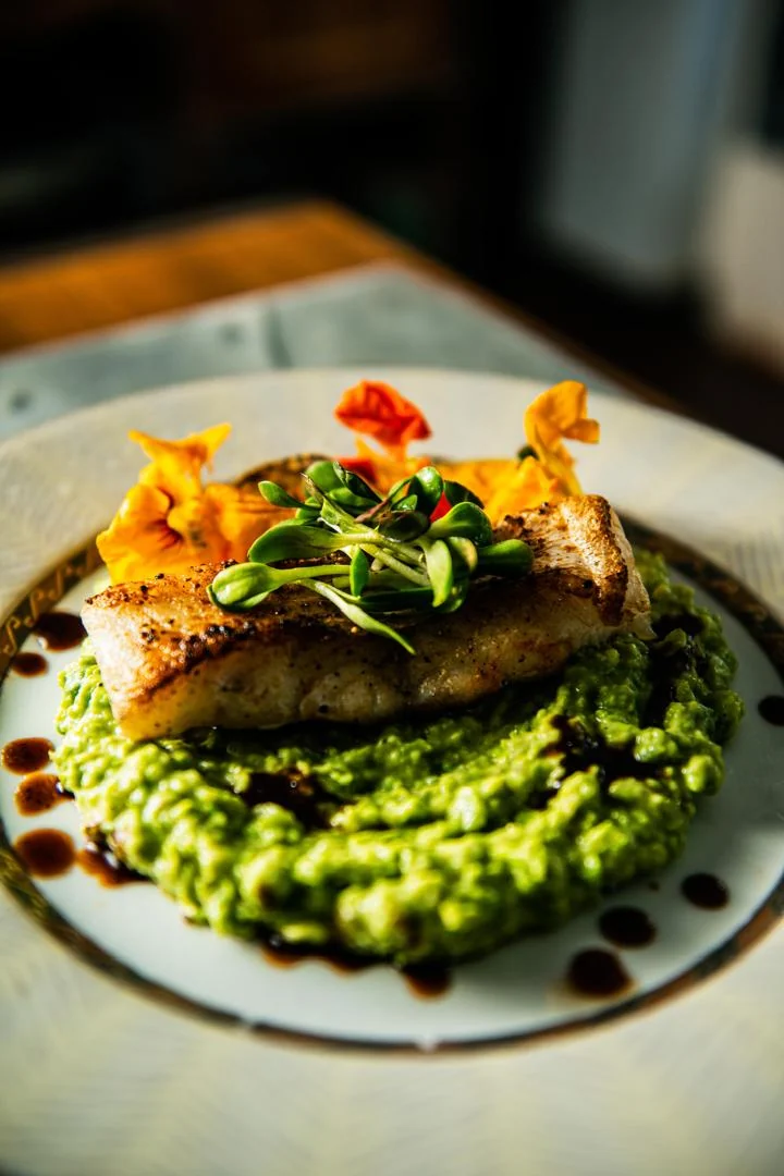 Pan-seared fish on a green purée, garnished with edible flowers and micro herbs
