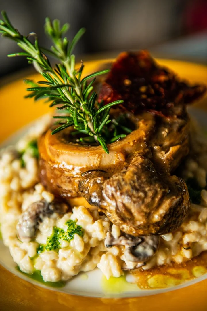 Slow-cooked meat topped with a sprig of rosemary on creamy risotto