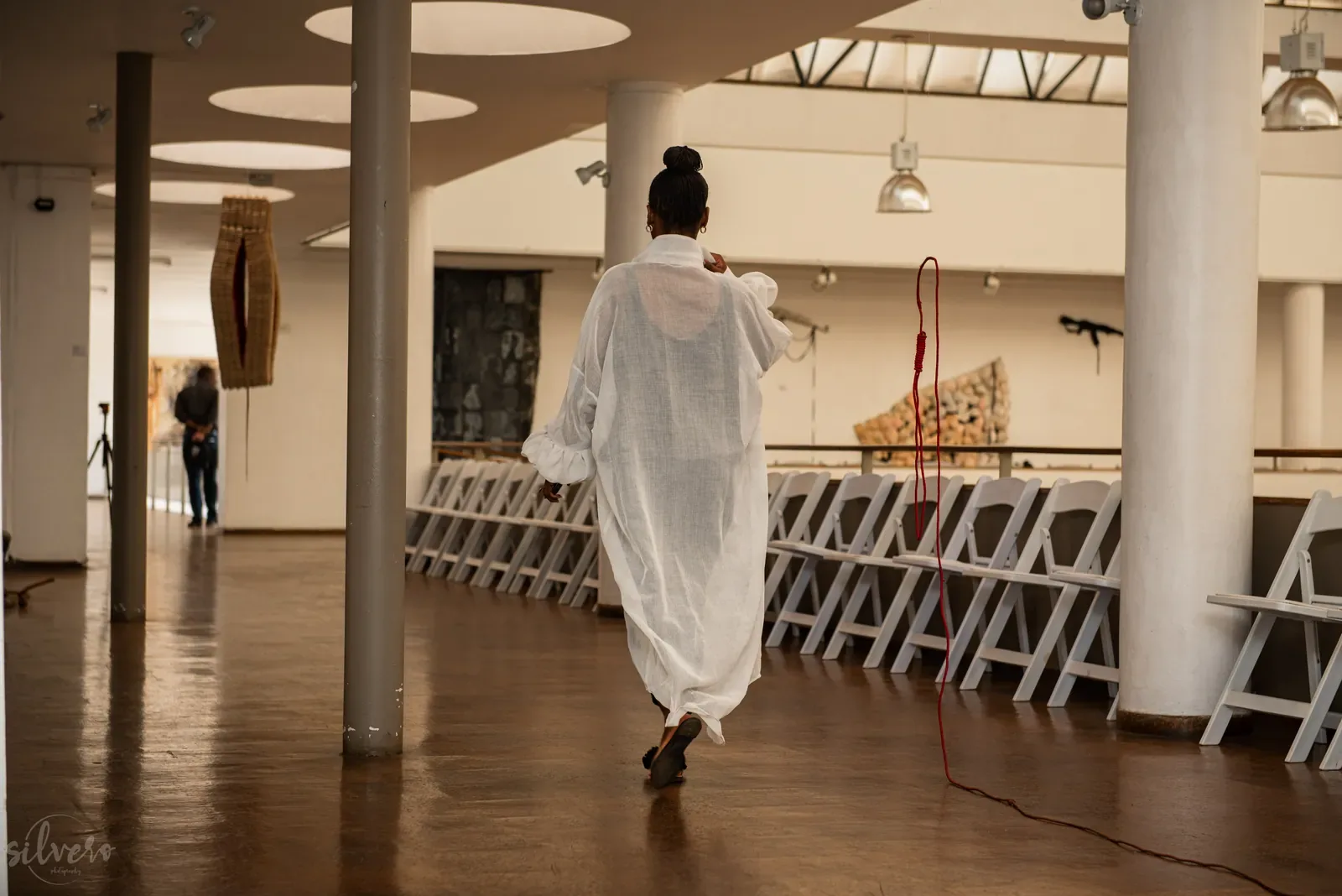 Model in a long white garment walking through a gallery hall