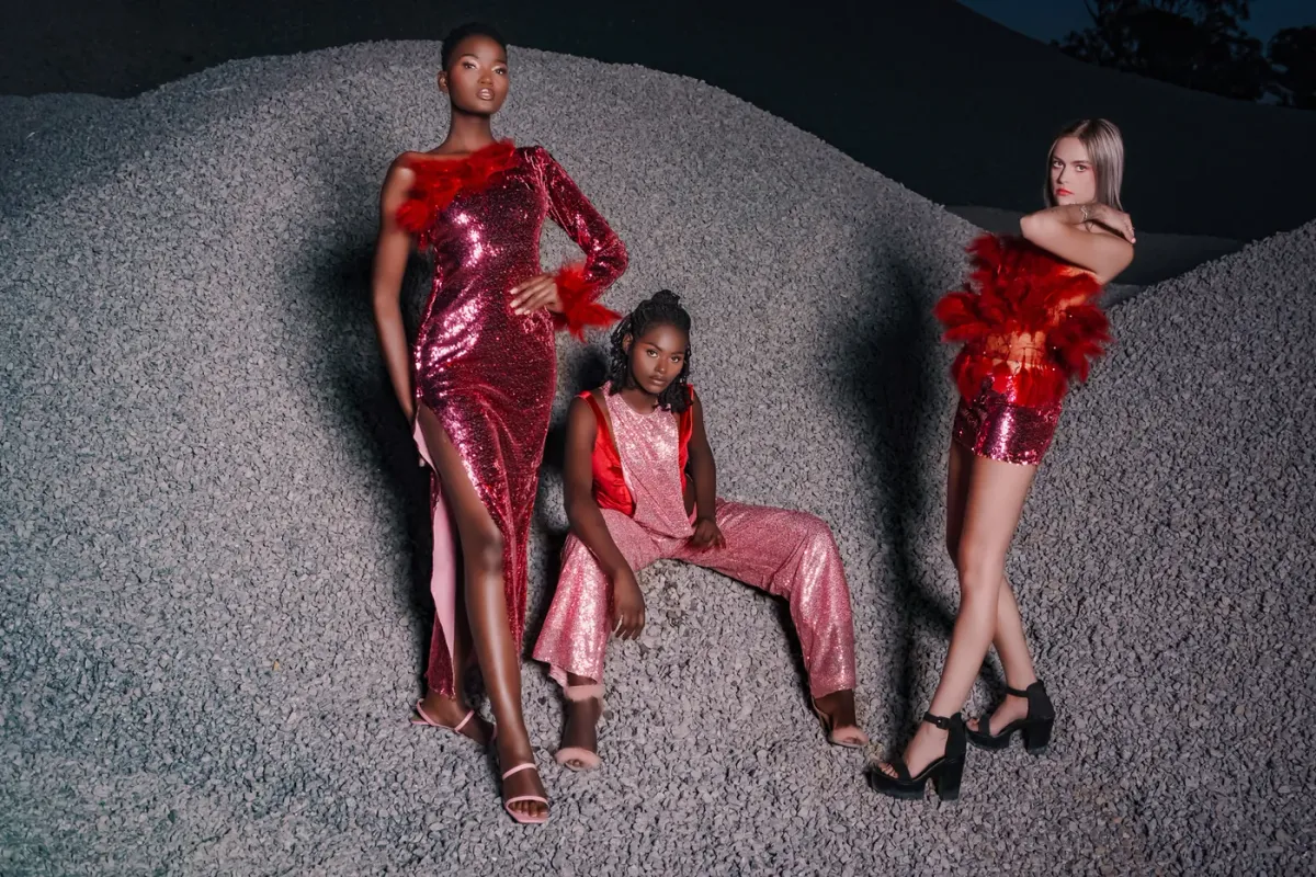 Three models in sequin outfits on a gravel hill